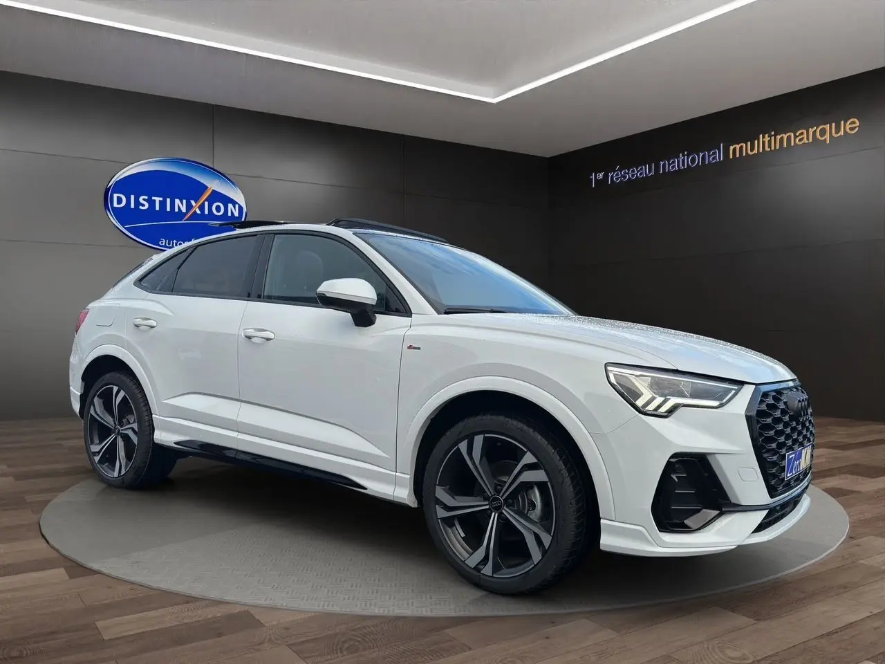 Audi Q3 Sportback blanc en 3/4 avant droit, avec jantes noires brillantes et toit panoramique visible.