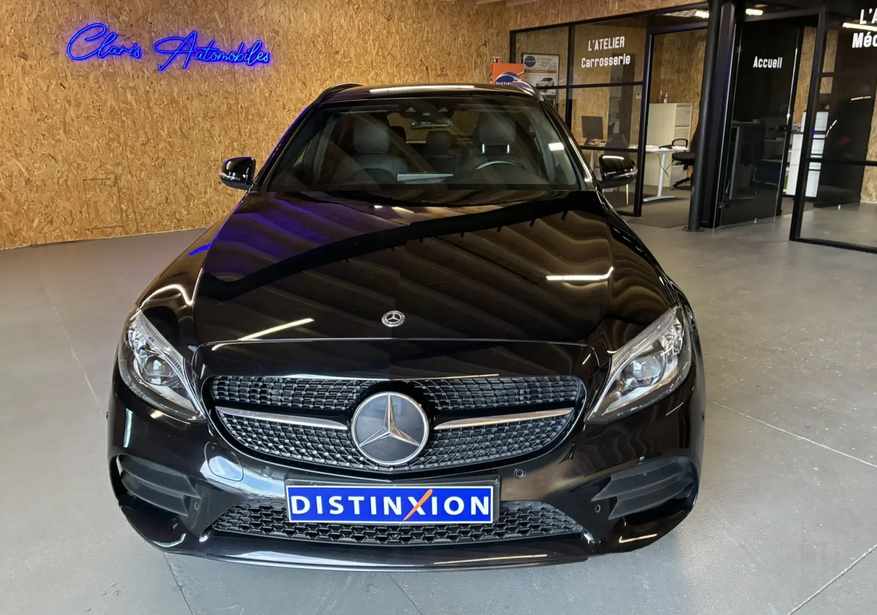 Vue avant d'une Mercedes Classe C Break 220D AMG Line noire métal, avec calandre distinctive et feux LED, en intérieur showroom.