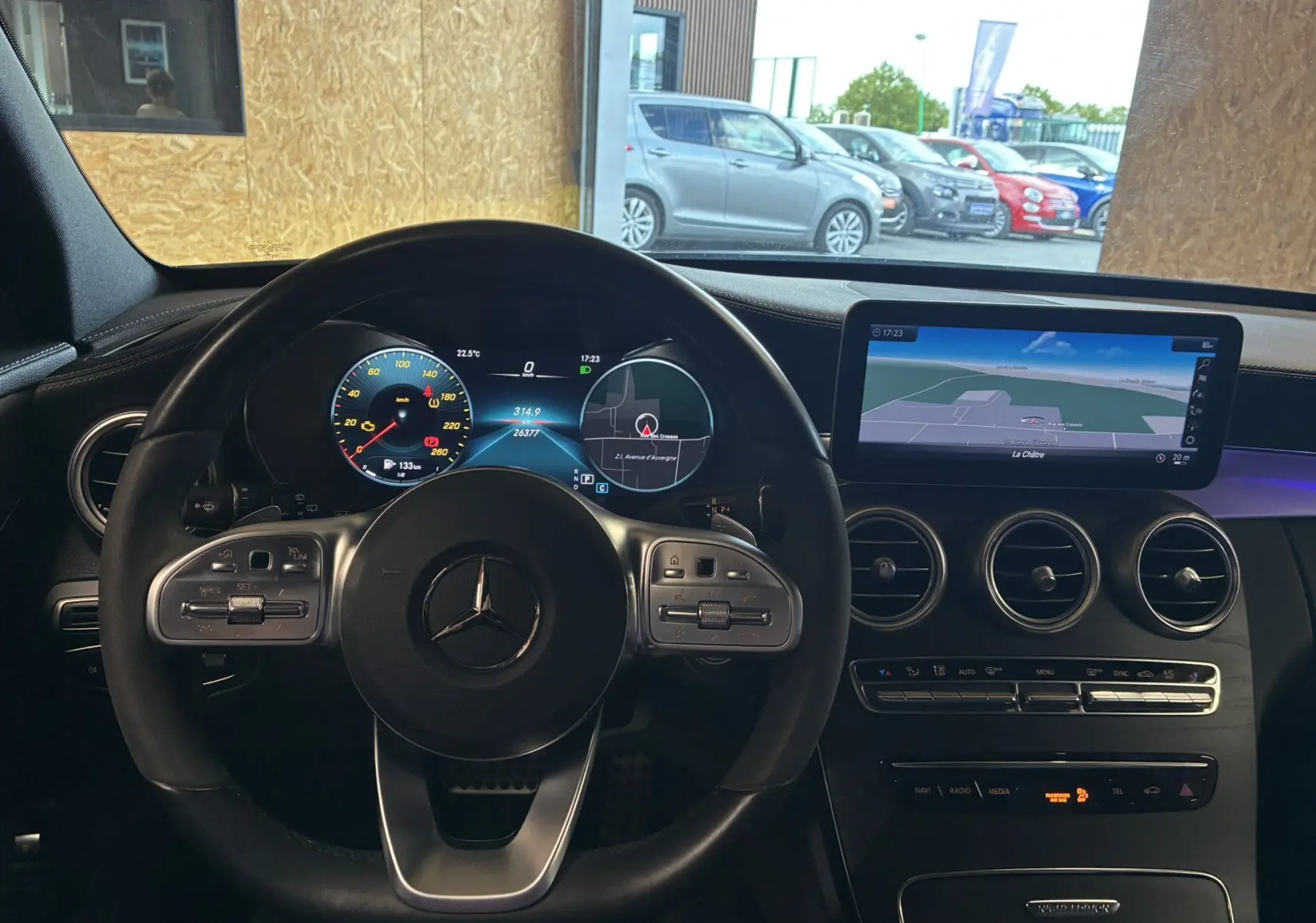 Vue intérieure centrée sur le volant cuir multifonction et l'écran tactile GPS de la Mercedes Classe C Break noir métal.