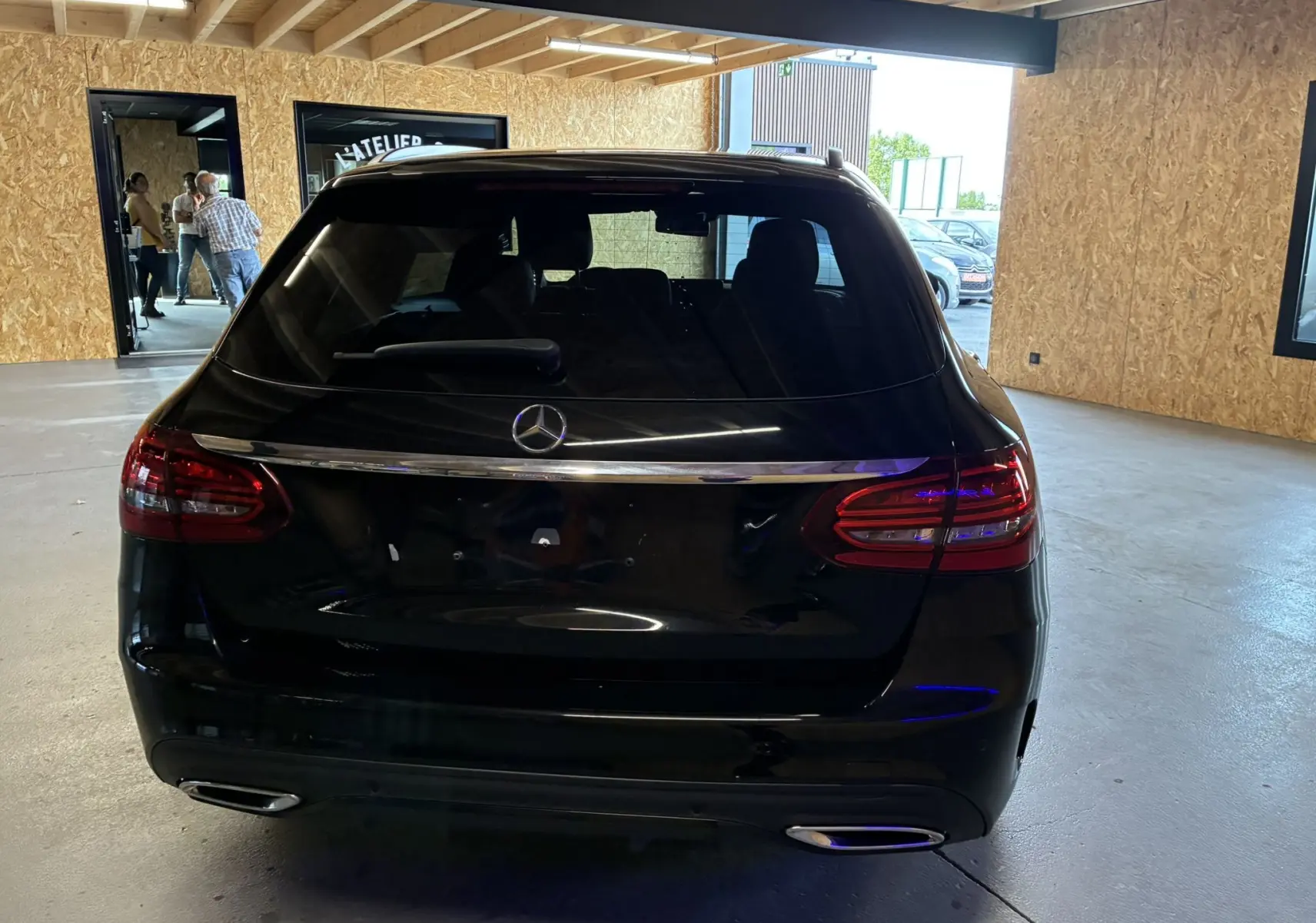 Vue arrière d'un Mercedes Classe C Break noir métal avec feux LED et double sortie d'échappement chromée en intérieur showroom.