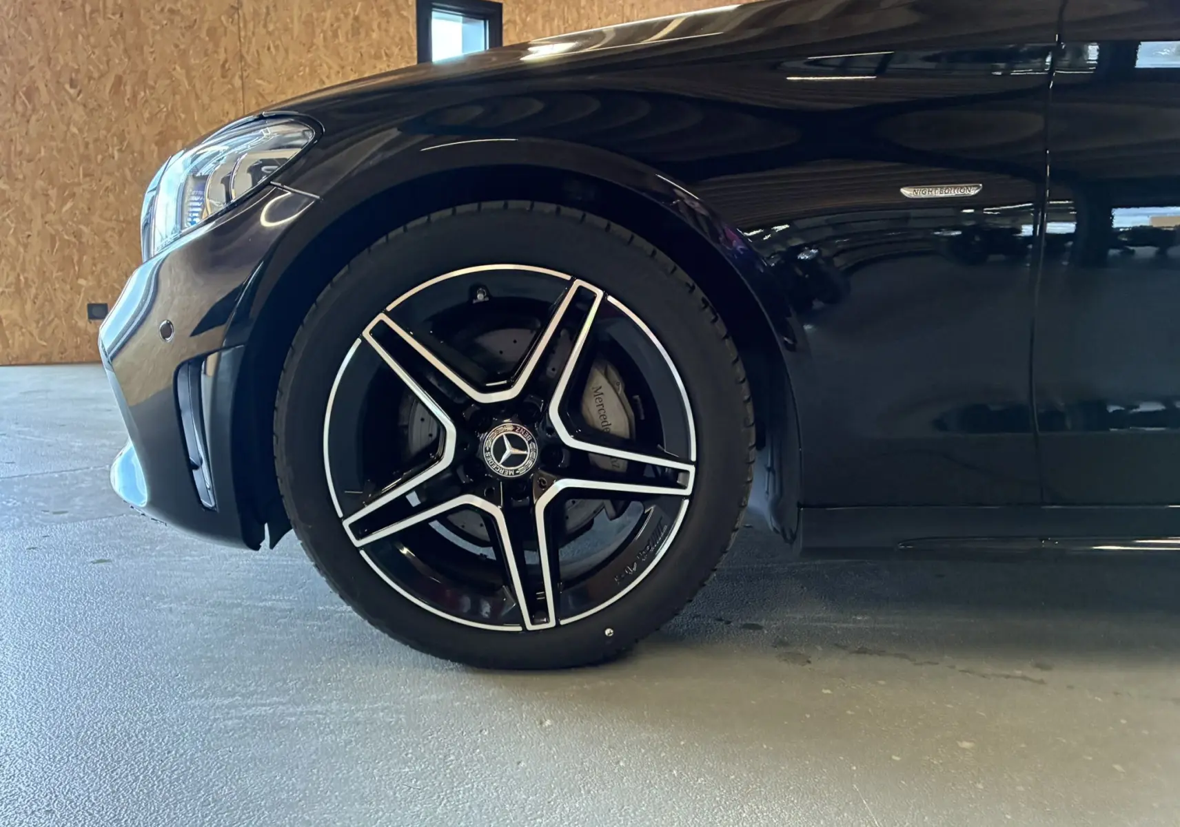 Gros plan sur la roue avant gauche et la partie avant noire métallisée d'une Mercedes Classe C Break AMG Line 2021.