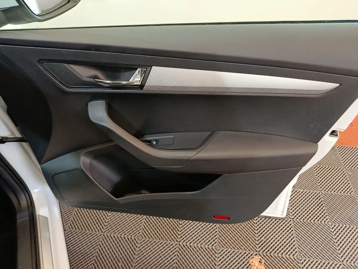 Vue intérieure côté gauche de la porte avant blanche du Skoda Karoq 2024 avec garniture noire et insert argenté.