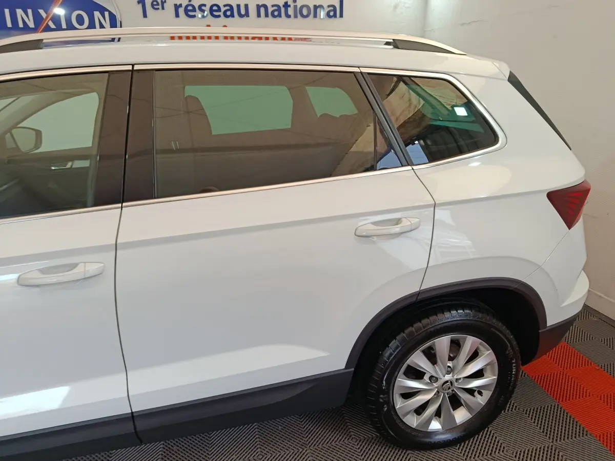 Vue latérale droite d'un Skoda Karoq blanc 2024, mettant en valeur la roue arrière et les vitres teintées.