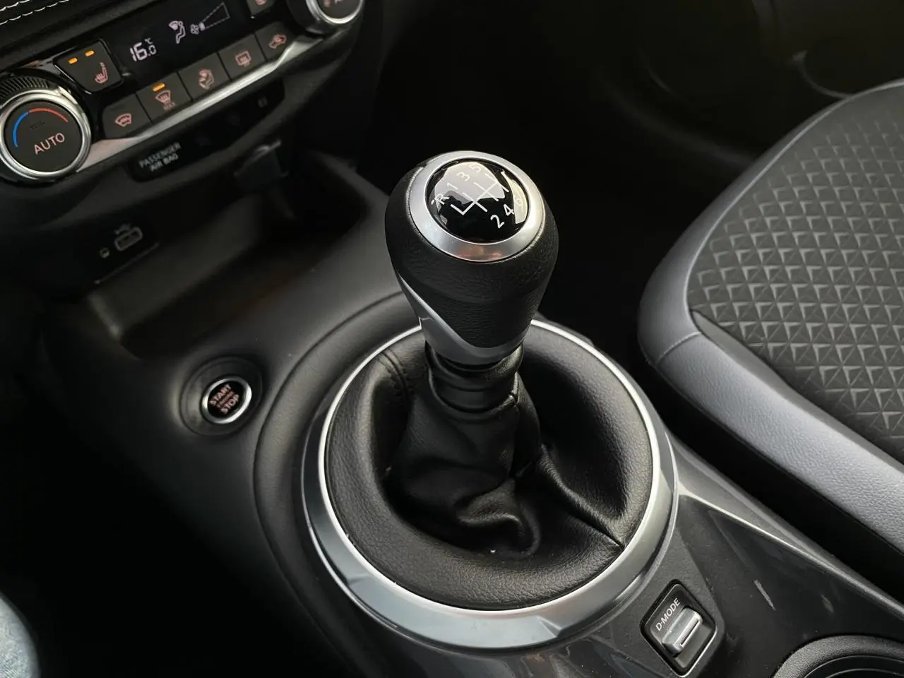 Gros plan sur le levier de vitesses manuel noir et argenté du Nissan Juke blanc perle, avec siège tissu gris à motifs.