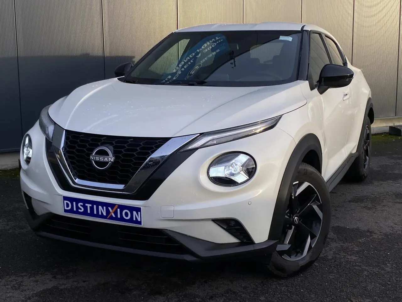 Nissan Juke blanc perle en 3/4 avant droit, avec calandre noire et jantes alliage noires distinctives.