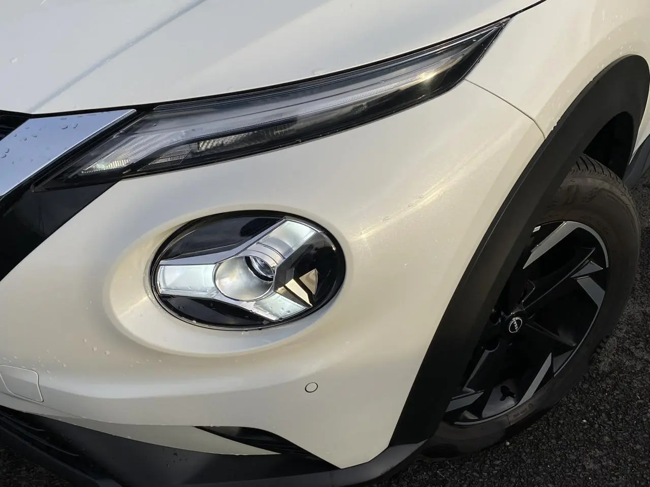 Gros plan sur le phare avant droit et la jante noire du Nissan Juke blanc perle 2024, version N-Connecta.