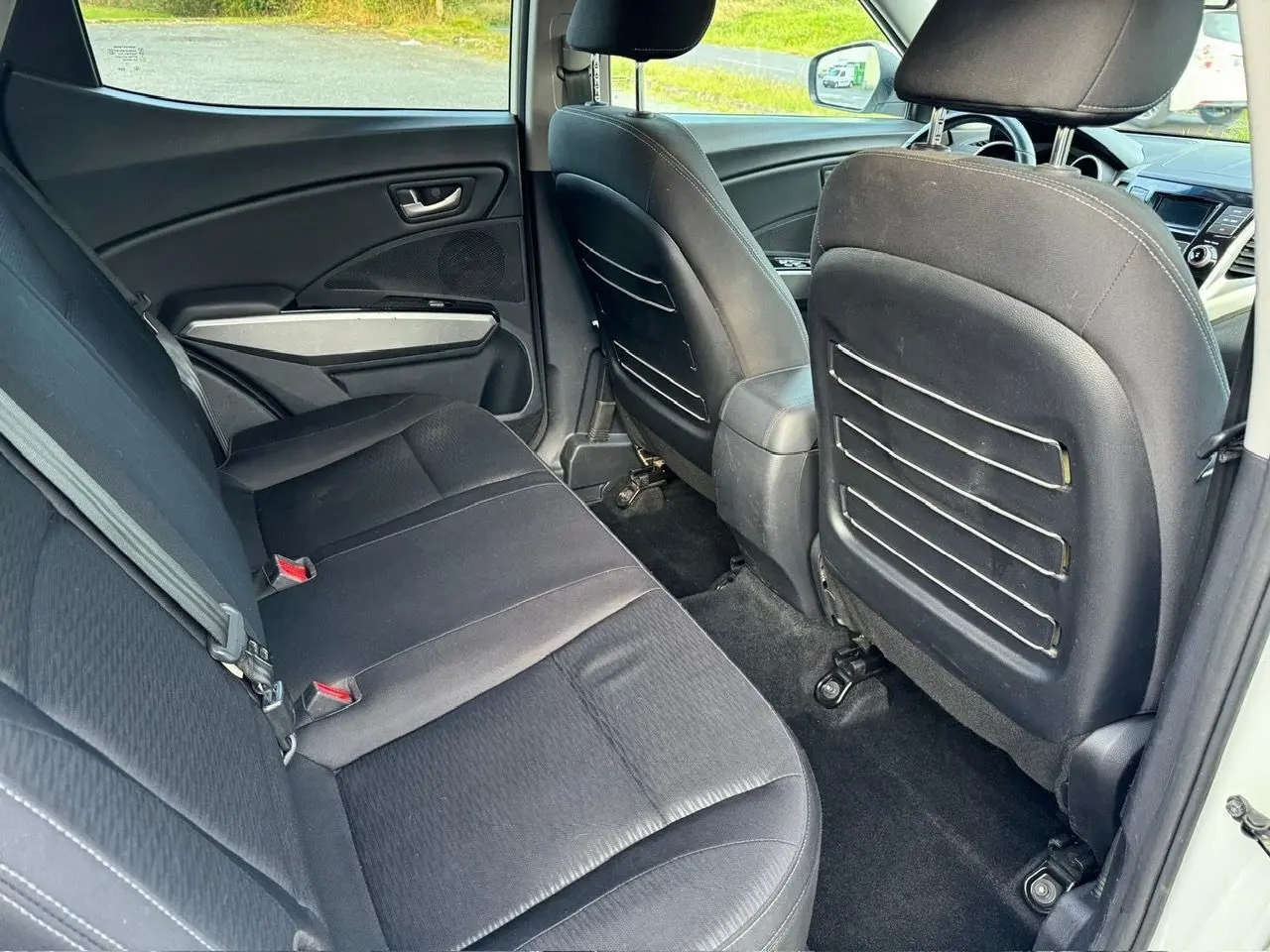 Vue intérieure arrière côté gauche du SSANGYONG TIVOLI blanc 2016, sièges noirs et rangements au dos des sièges avant.