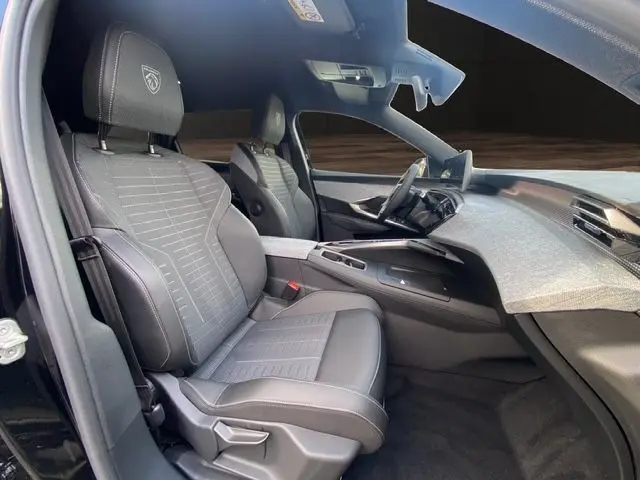 Intérieur avant du Peugeot 5008 noir Perla, sièges cuir gris noir avec logo Peugeot brodé et tableau de bord moderne.