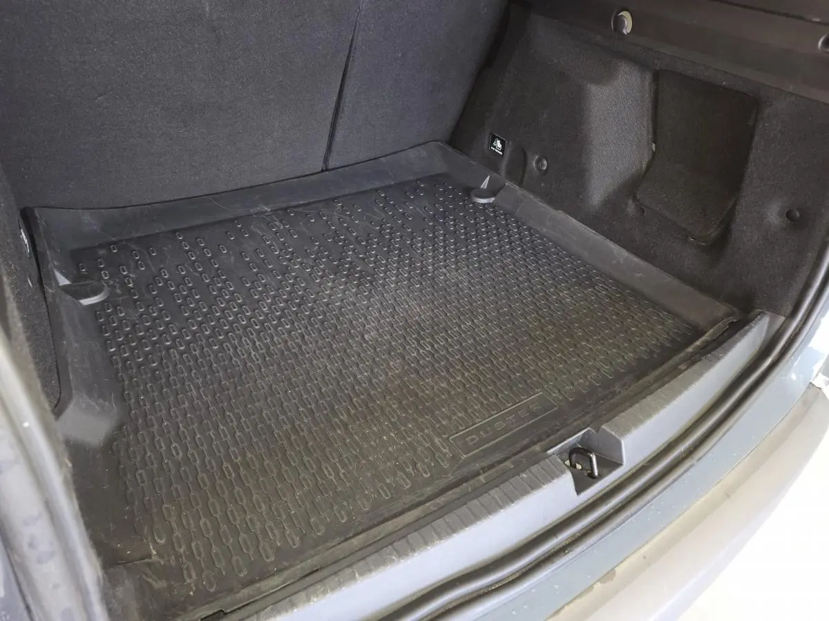 Vue rapprochée de la malle arrière grise du Dacia Duster 2024 avec tapis de coffre noir marqué Duster.