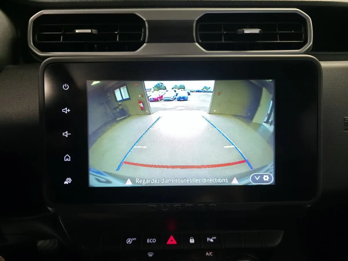 Écran tactile intérieur du Dacia Duster 2024 montrant la caméra de recul avec lignes de guidage bleues et rouges.