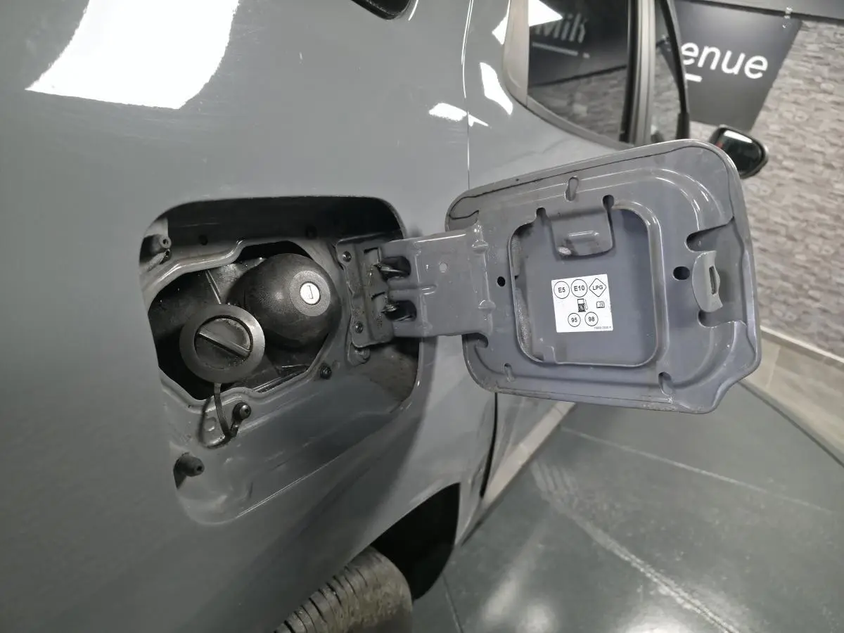 Gros plan sur la trappe à carburant ouverte côté gauche d’un Dacia Duster gris urbain 2024, montrant les bouchons essence et GPL.