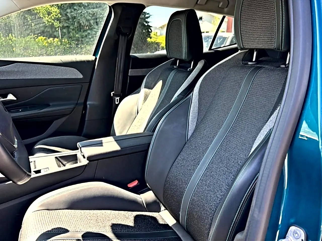 Vue intérieure côté conducteur de la Peugeot 408 Hybrid 145 allure e-dcs6 bleu, sièges tissu et cuir avec accoudoir central.