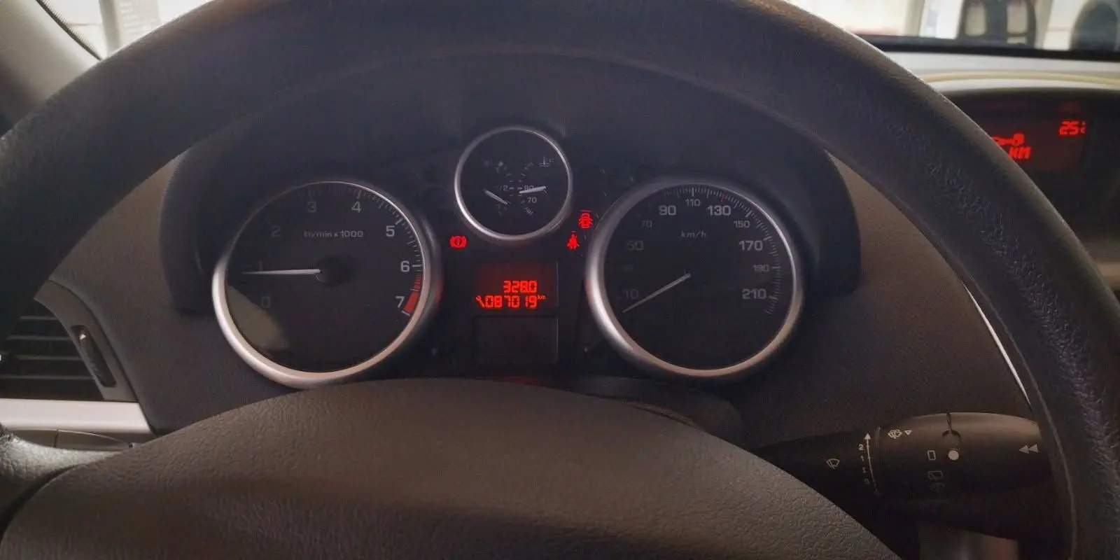 Vue rapprochée du tableau de bord et du volant noir d'une Peugeot 207+ 1.4l HDi 2013 avec compteurs analogiques.