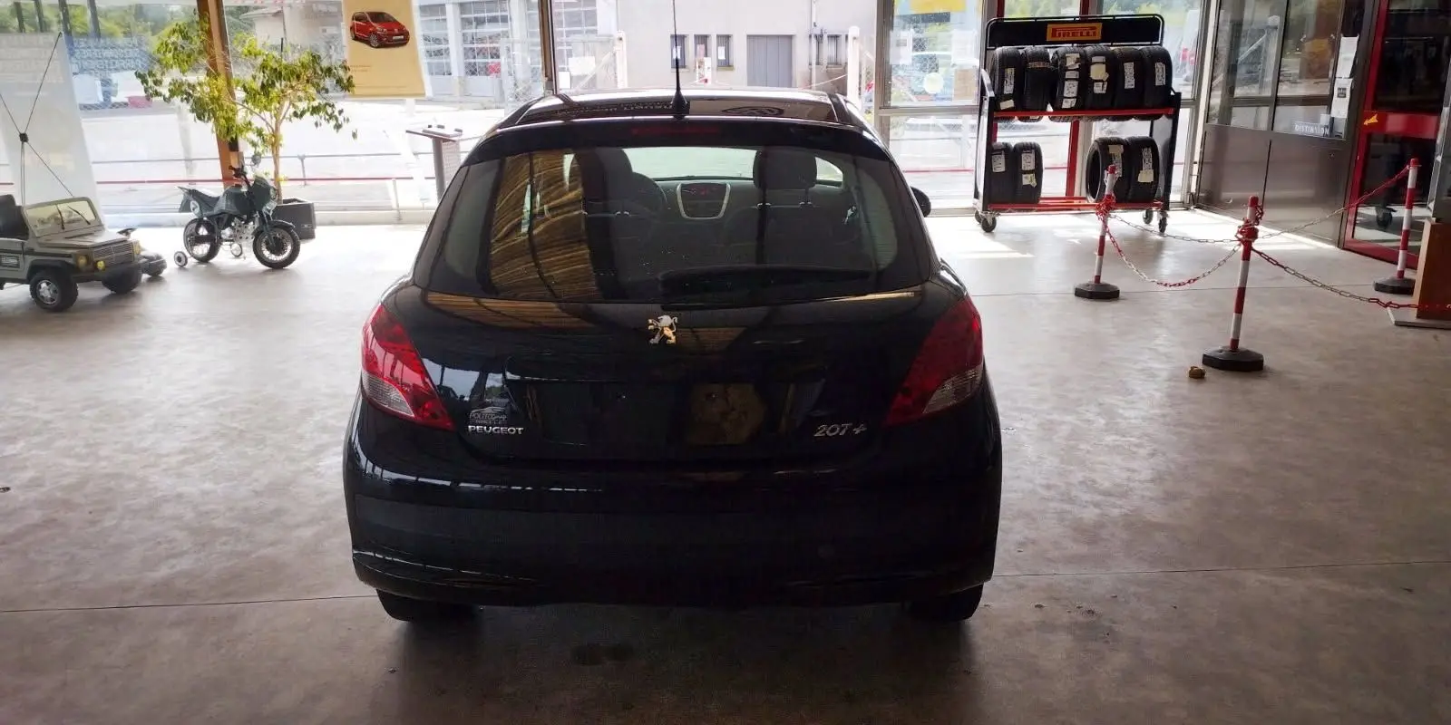 Vue arrière d'une Peugeot 207+ noire de 2013, avec logo et badges visibles dans un garage lumineux.