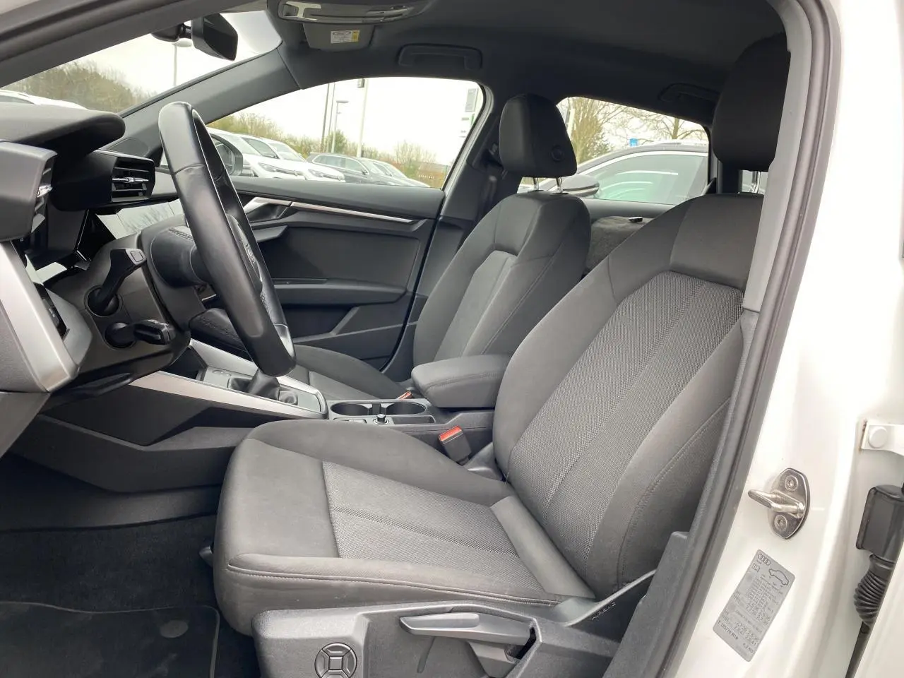 Vue intérieure côté conducteur de l'Audi A3 Sportback blanc Ibis 2022 avec sièges tissu gris et volant cuir.