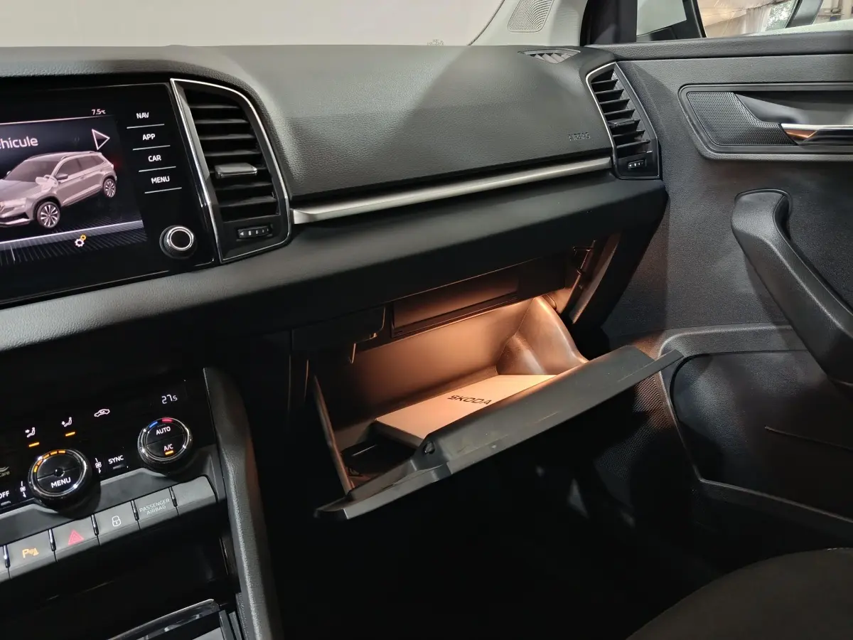 Intérieur de la Skoda Karoq 2024, vue côté passager sur la boîte à gants ouverte avec éclairage intérieur et écran tactile central.