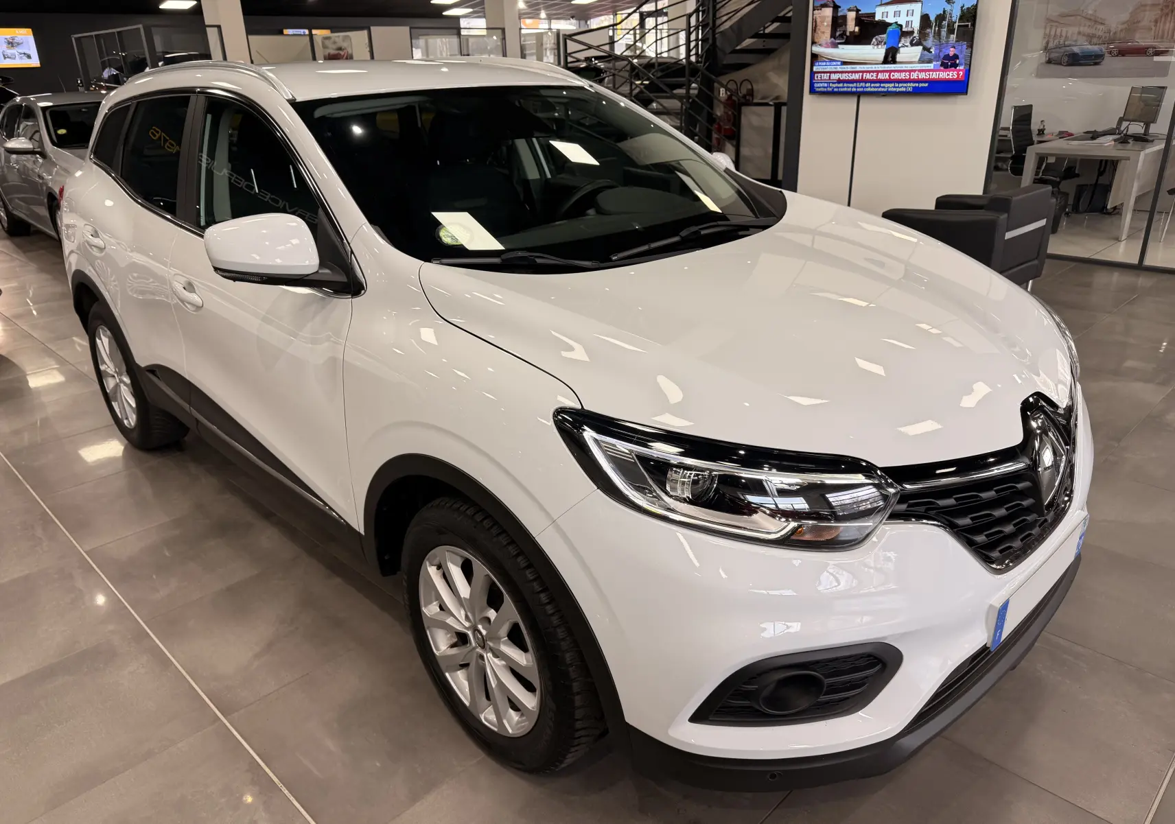 Renault Kadjar blanc Glacier en vue 3/4 avant droit, avec calandre noire et phares LED dans un showroom.