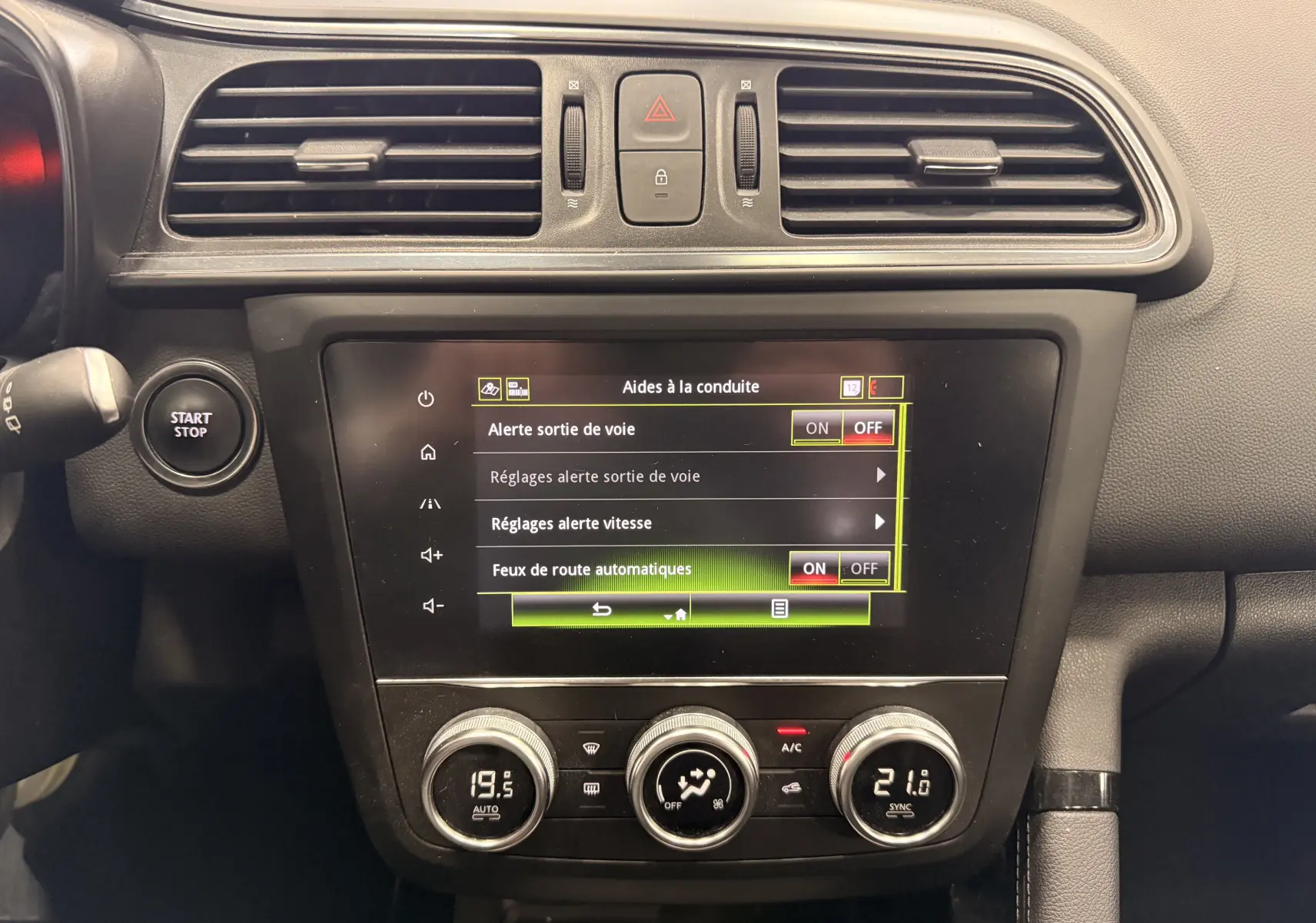 Vue rapprochée du tableau de bord du Renault Kadjar blanc, affichant l'écran tactile des aides à la conduite et les commandes de climatisation.