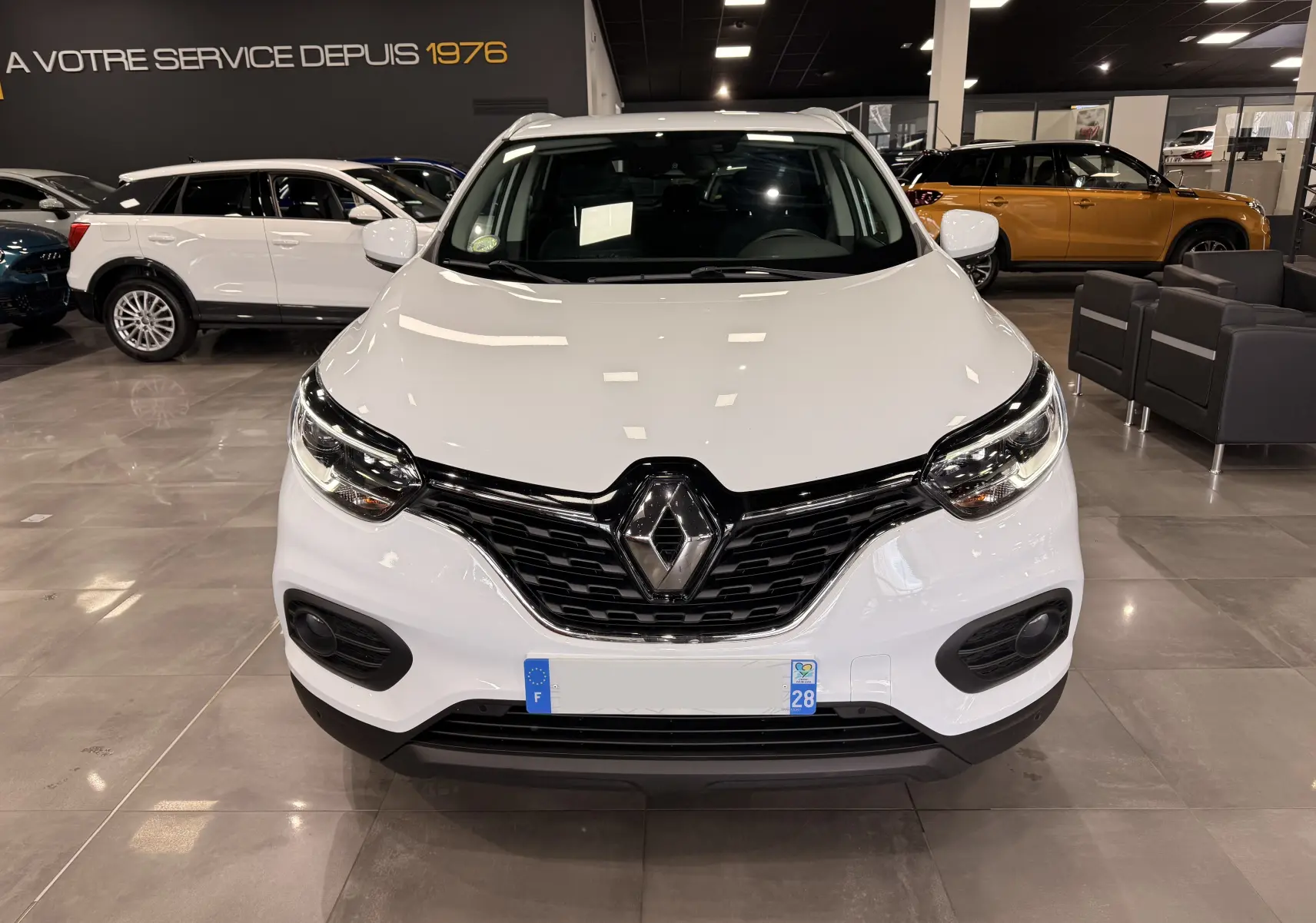 Vue de face d'un Renault Kadjar blanc Glacier 2020 dans un showroom, avec calandre noire et logo Renault bien visible.