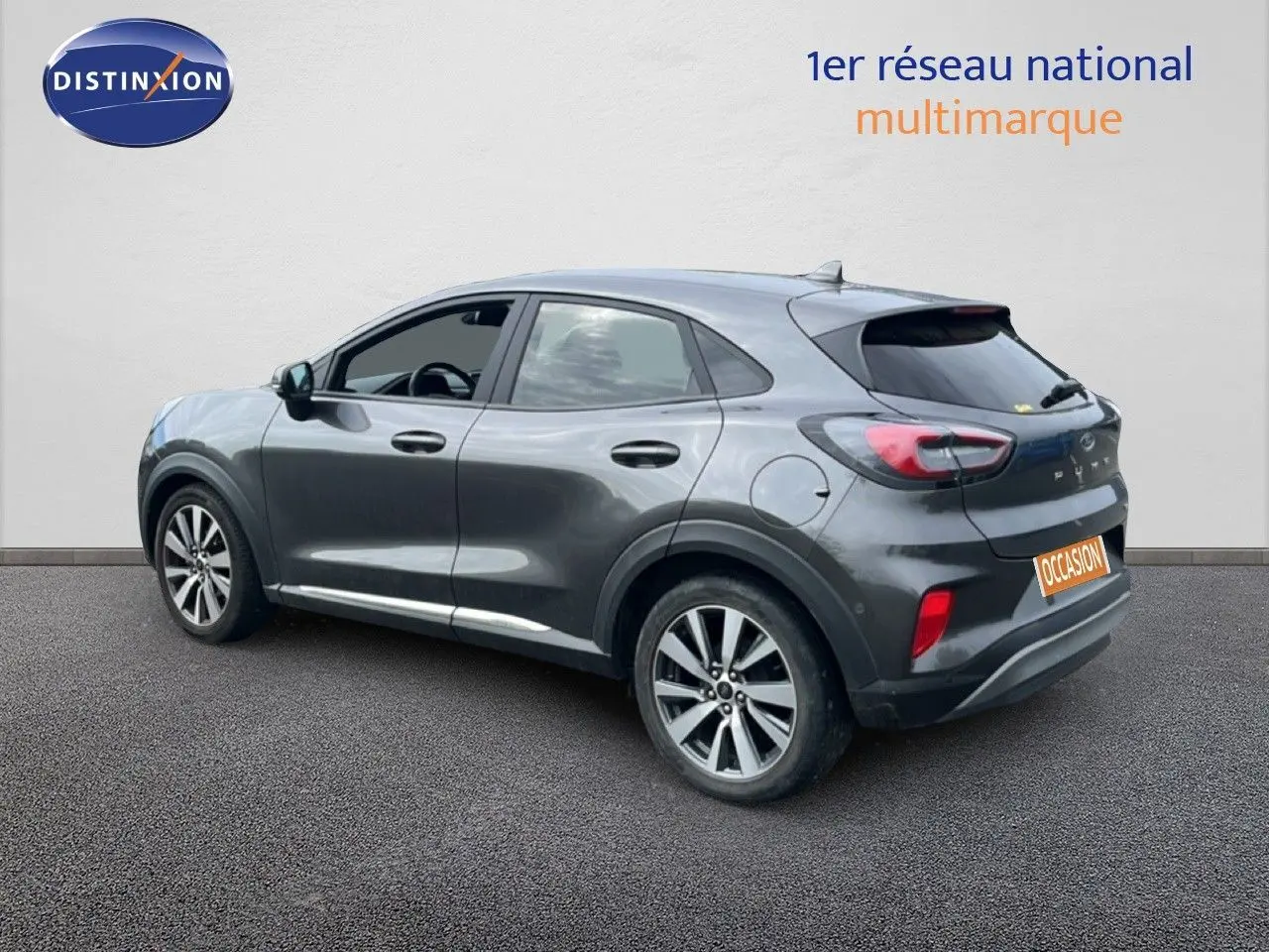 Ford Puma gris en vue 3/4 arrière droit, avec jantes alliage et vitres teintées, stationné devant un mur blanc.