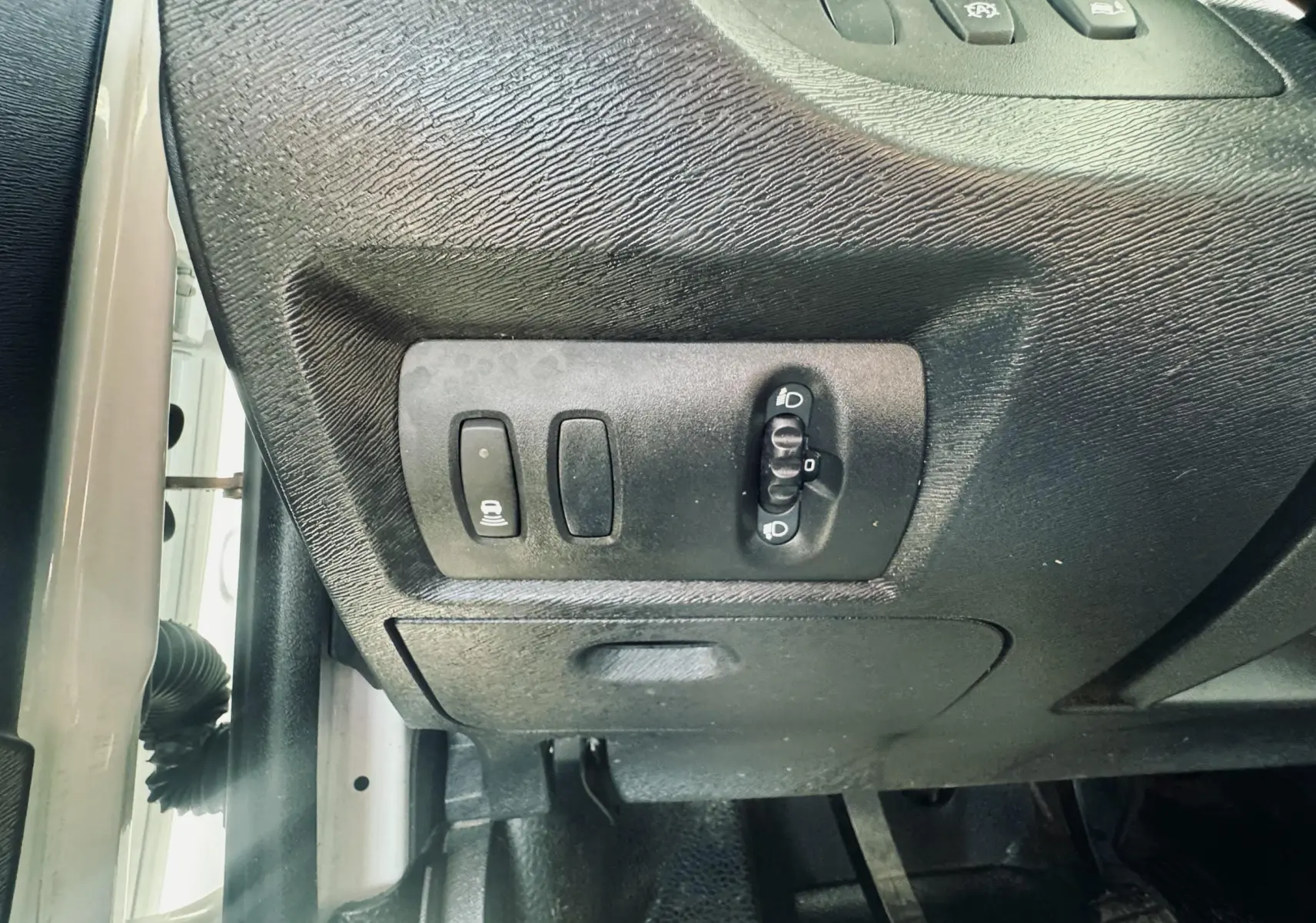 Vue rapprochée des commandes d’éclairage et réglage des phares sur le côté gauche du tableau de bord du Renault Kangoo blanc.