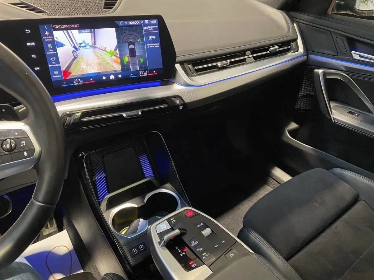 Vue intérieure côté passager du tableau de bord et console centrale du BMW X1 noir avec écran tactile et éclairage d’ambiance bleu.