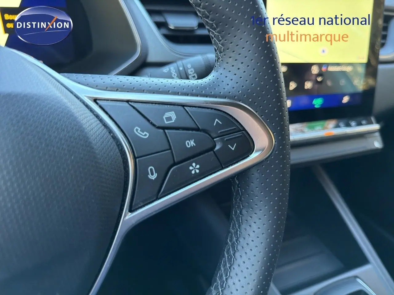Gros plan sur la partie gauche du volant en cuir perforé noir du Renault Symbioz 2025, avec commandes intégrées et écran tactile flou en arrière-plan.
