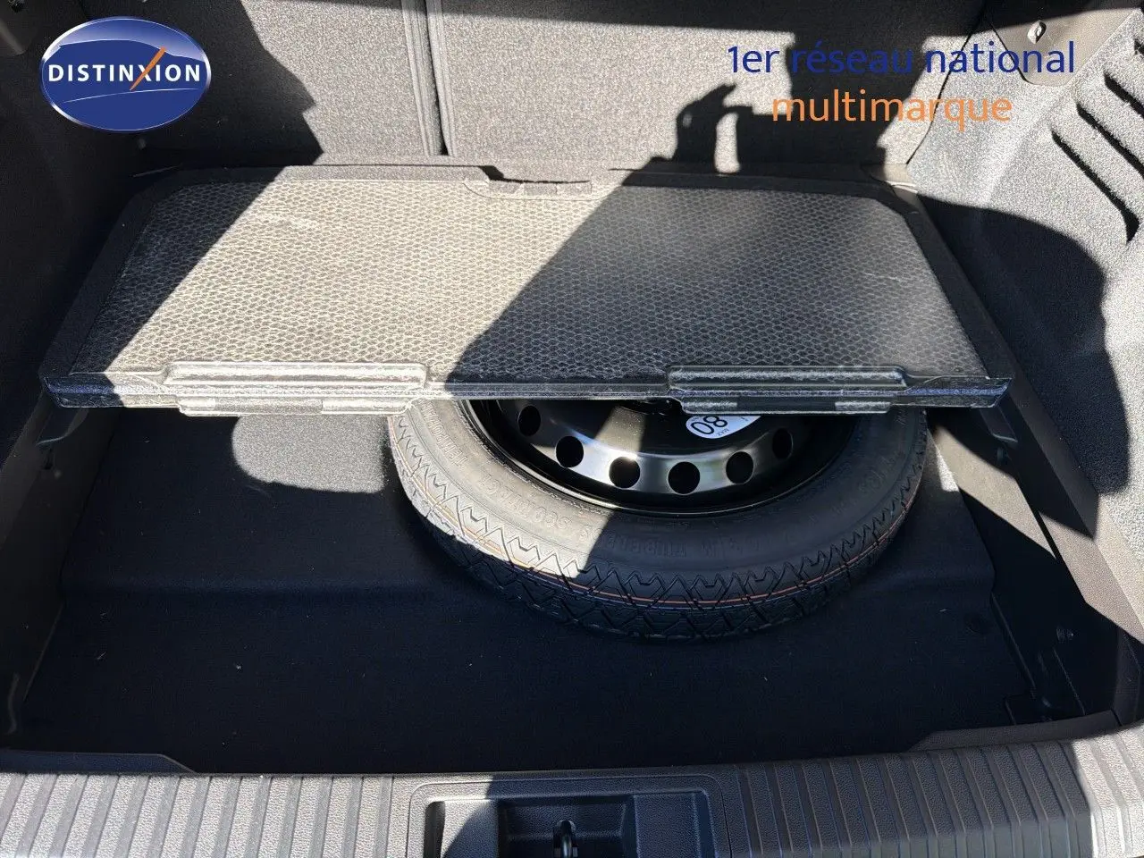 Vue plongeante sur le coffre ouvert du Renault Symbioz gris Rafale, montrant la roue de secours sous la tablette amovible.