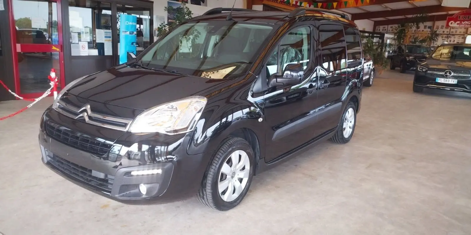 Citroën Berlingo noir en 3/4 avant droit, montrant ses phares et la calandre dans un showroom intérieur.