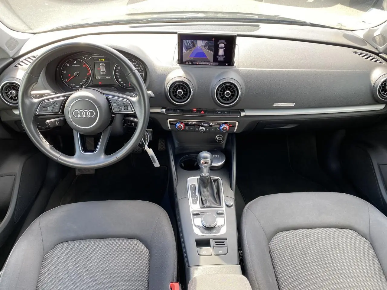 Vue intérieure avant de l'Audi A3 Sportback 2020, tableau de bord noir avec écran central et volant multifonction.
