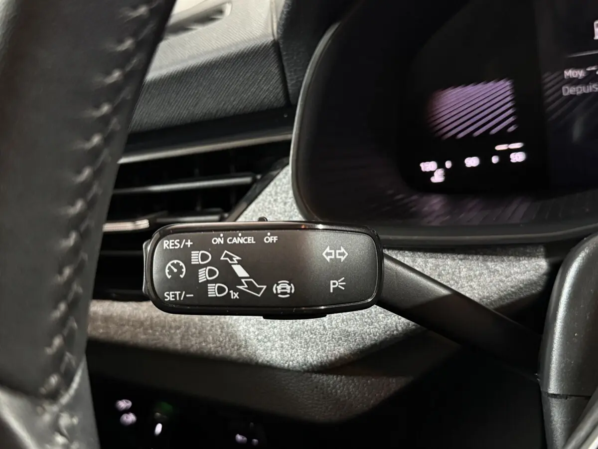 Gros plan sur la commande de régulateur de vitesse au volant cuir du Skoda Kamiq rouge, tableau de bord en arrière-plan.