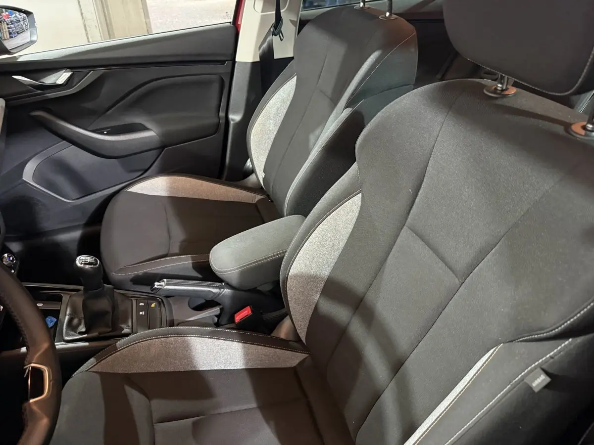 Vue intérieure côté conducteur du Skoda Kamiq rouge 2024, sièges tissu bicolore avec accoudoir central et boîte manuelle.