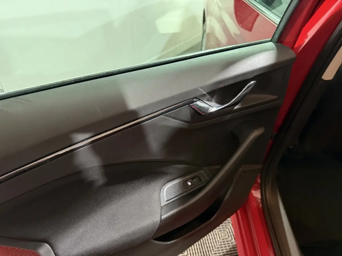 Vue rapprochée de la porte avant gauche rouge d’un Skoda Kamiq 2024 avec poignée chromée et commande de vitre électrique.