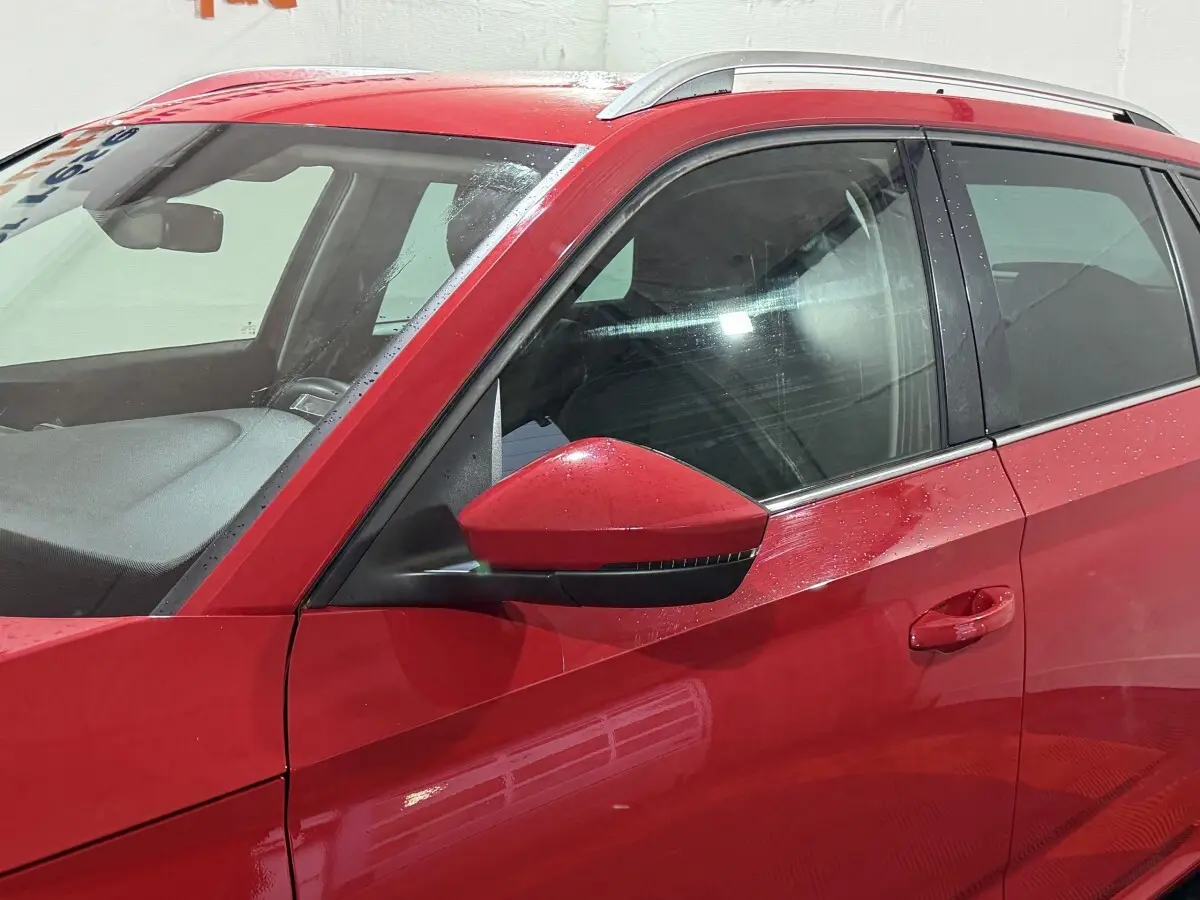 Vue latérale côté gauche d’un Skoda Kamiq rouge avec rétroviseur assorti et barres de toit argentées.