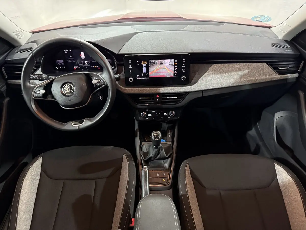 Vue intérieure frontale du Skoda Kamiq rouge 2024, volant cuir multifonctions et écran tactile central allumé.