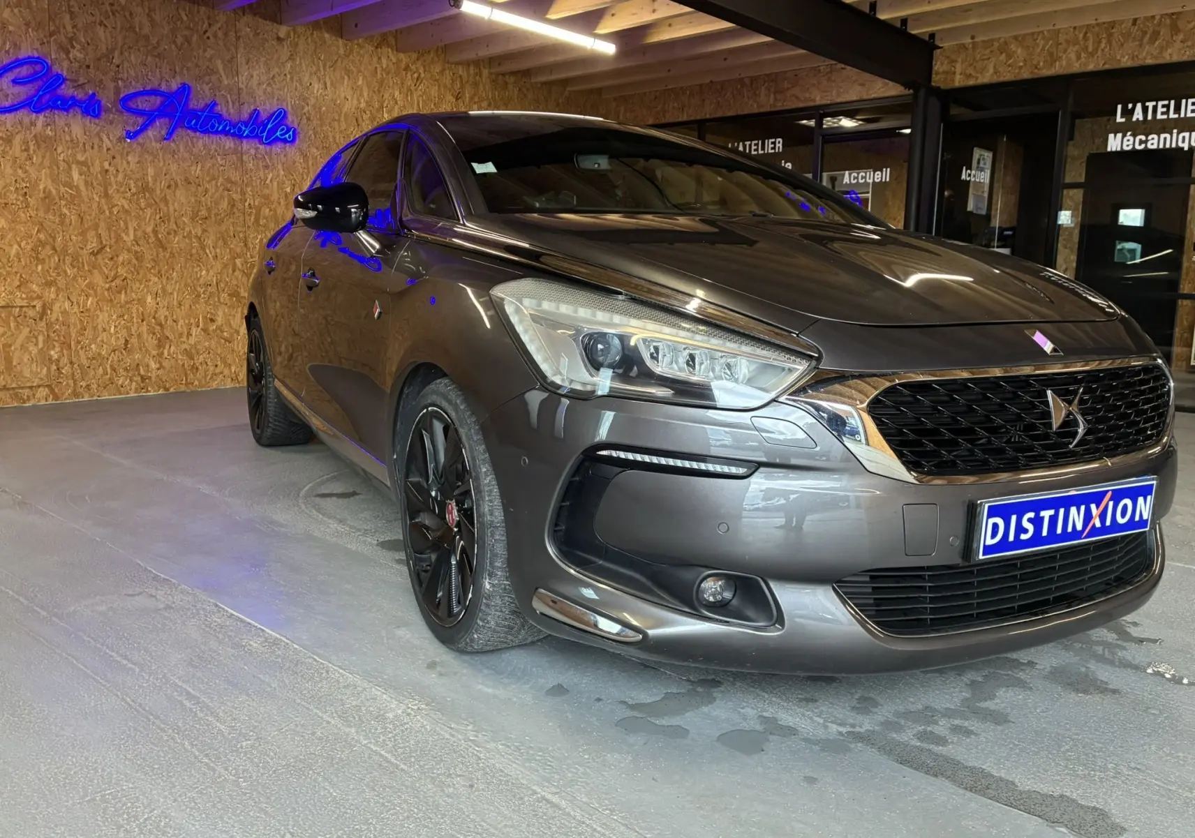 DS5 gris 3/4 avant droit, avec jantes noires et calandre distinctive DS, dans un showroom intérieur.