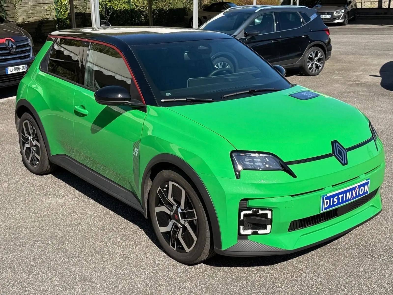 Vue 3/4 avant droit d'une Renault R5 E-Tech électrique vert Pop avec toit noir étoile et jonc de toit rouge alu.