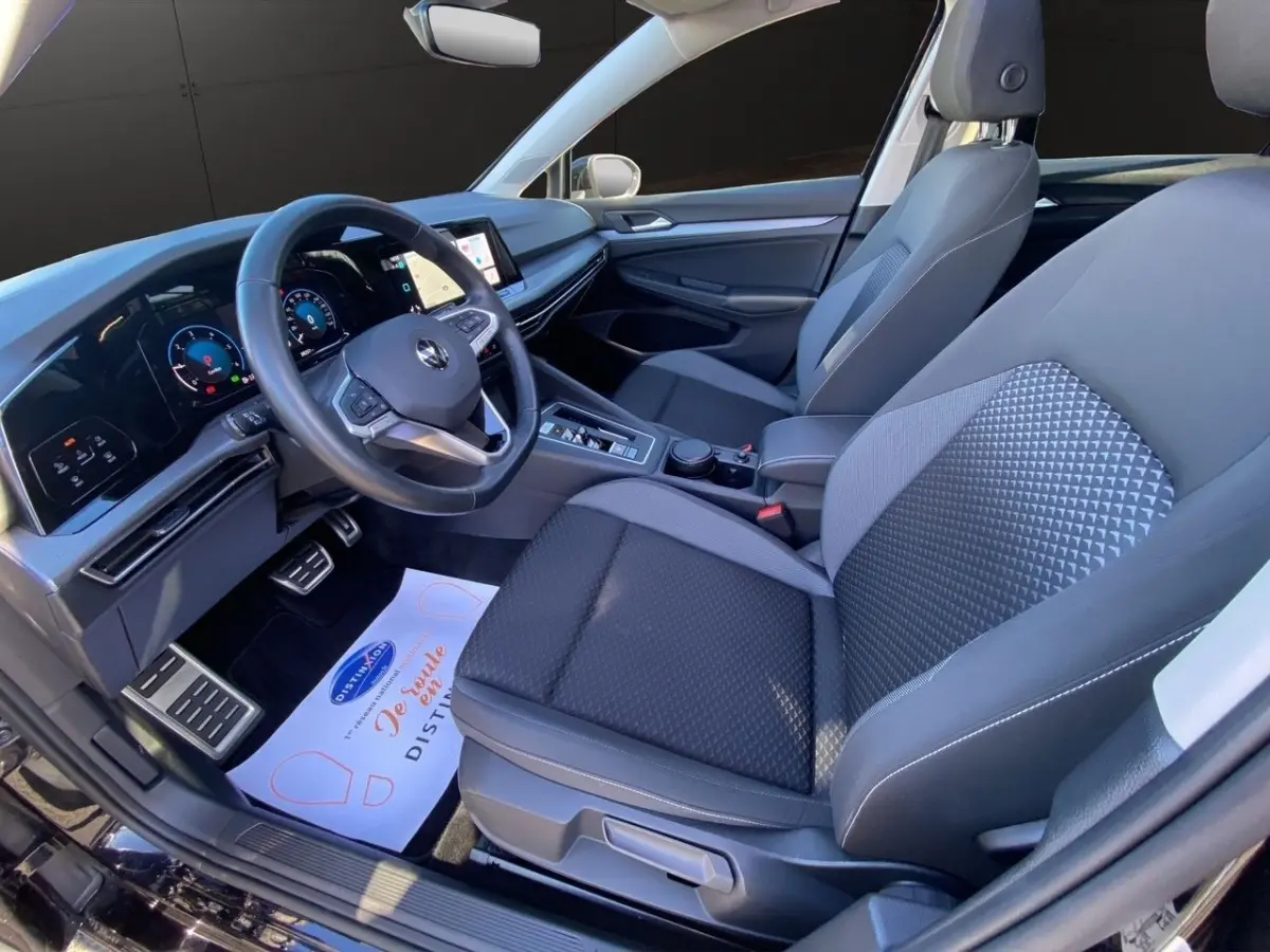 Vue intérieure côté conducteur de la Volkswagen Golf noire 2022, avec tableau de bord digital et sièges tissu gris.