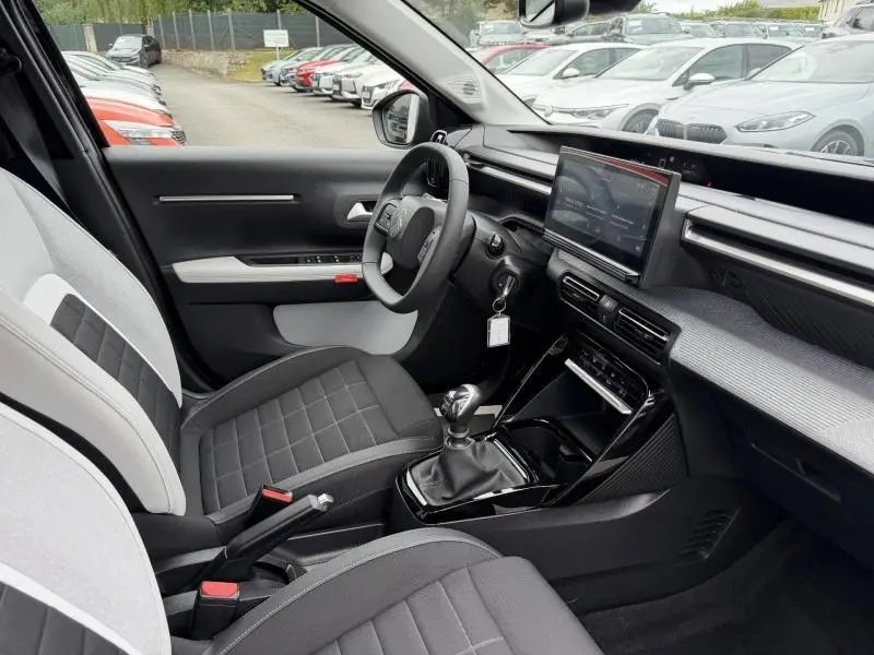 Intérieur de la Citroën C3 2025 en vue côté conducteur, sièges tissu noir et gris, tableau de bord avec écran tactile.