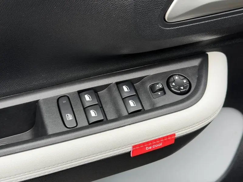 Gros plan sur les commandes de vitres et rétroviseurs côté conducteur de la Citroën C3 2025 en Noir Perla Nera avec surpiqûre blanche et étiquette rouge "be cool".