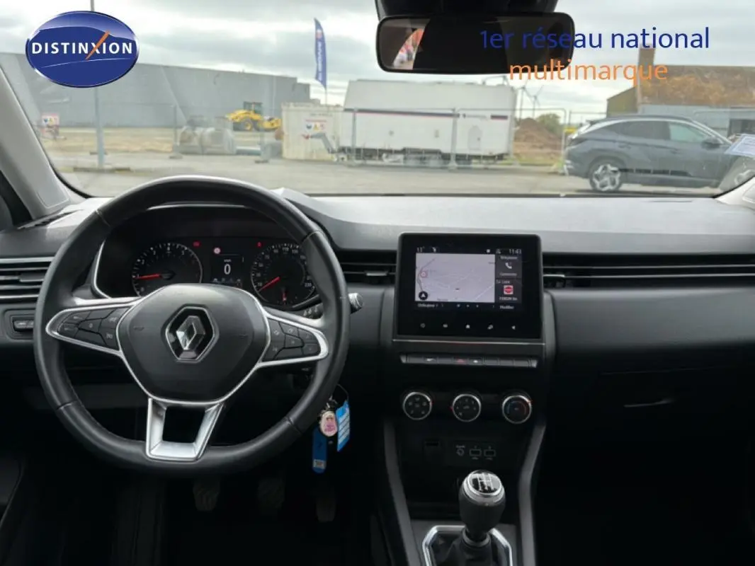 Vue intérieure frontale du tableau de bord et volant noir d'une Renault Clio blanche, avec écran tactile et boîte manuelle.