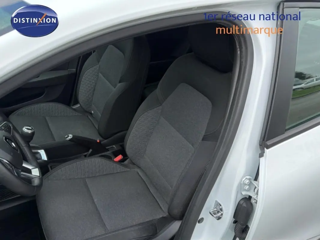 Vue intérieure côté conducteur de la Renault Clio blanc 2021, montrant les sièges en tissu gris et la boîte manuelle.