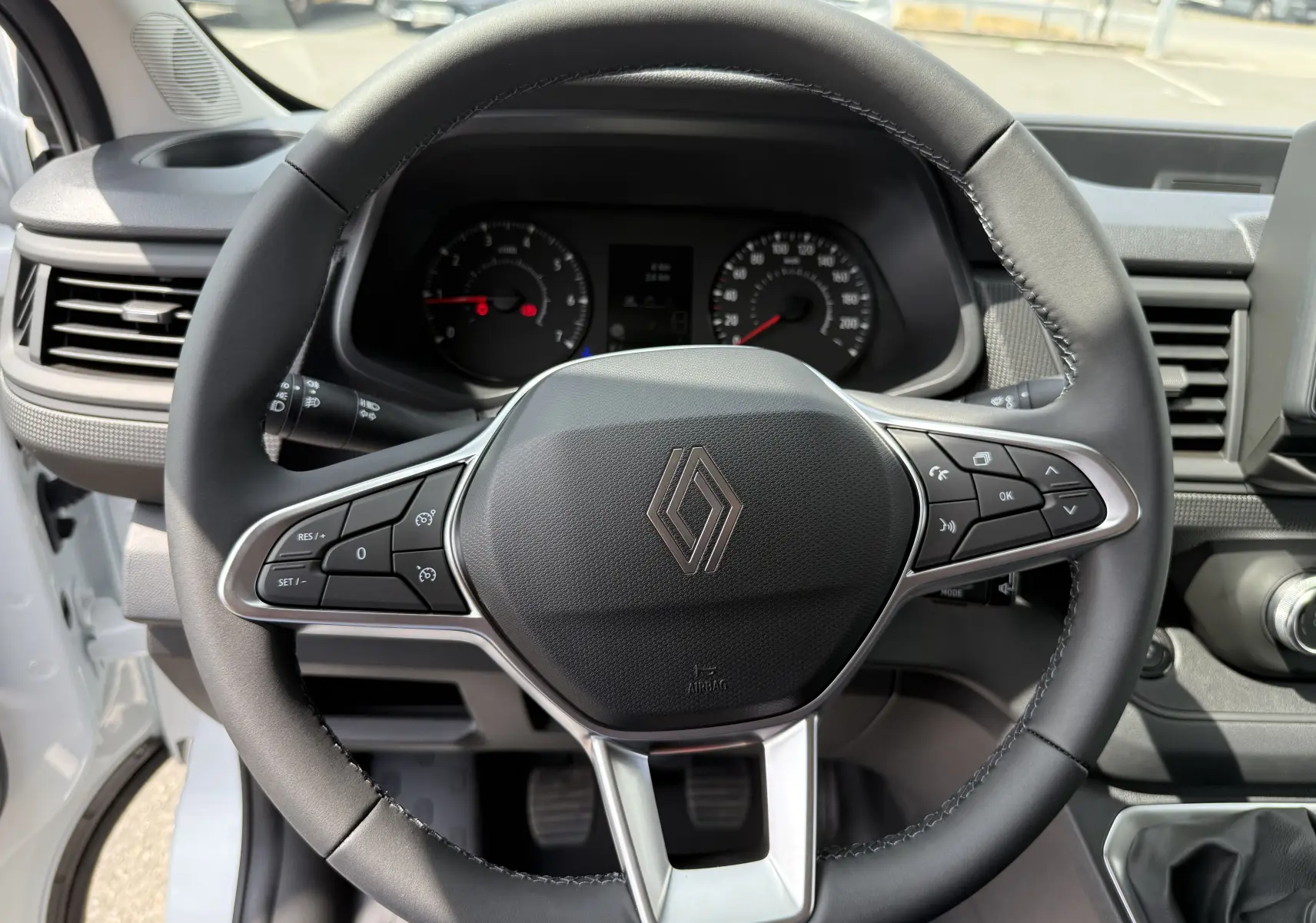 Vue rapprochée du volant noir du Renault Trafic Fourgon blanc 2025 avec commandes intégrées et tableau de bord visible.
