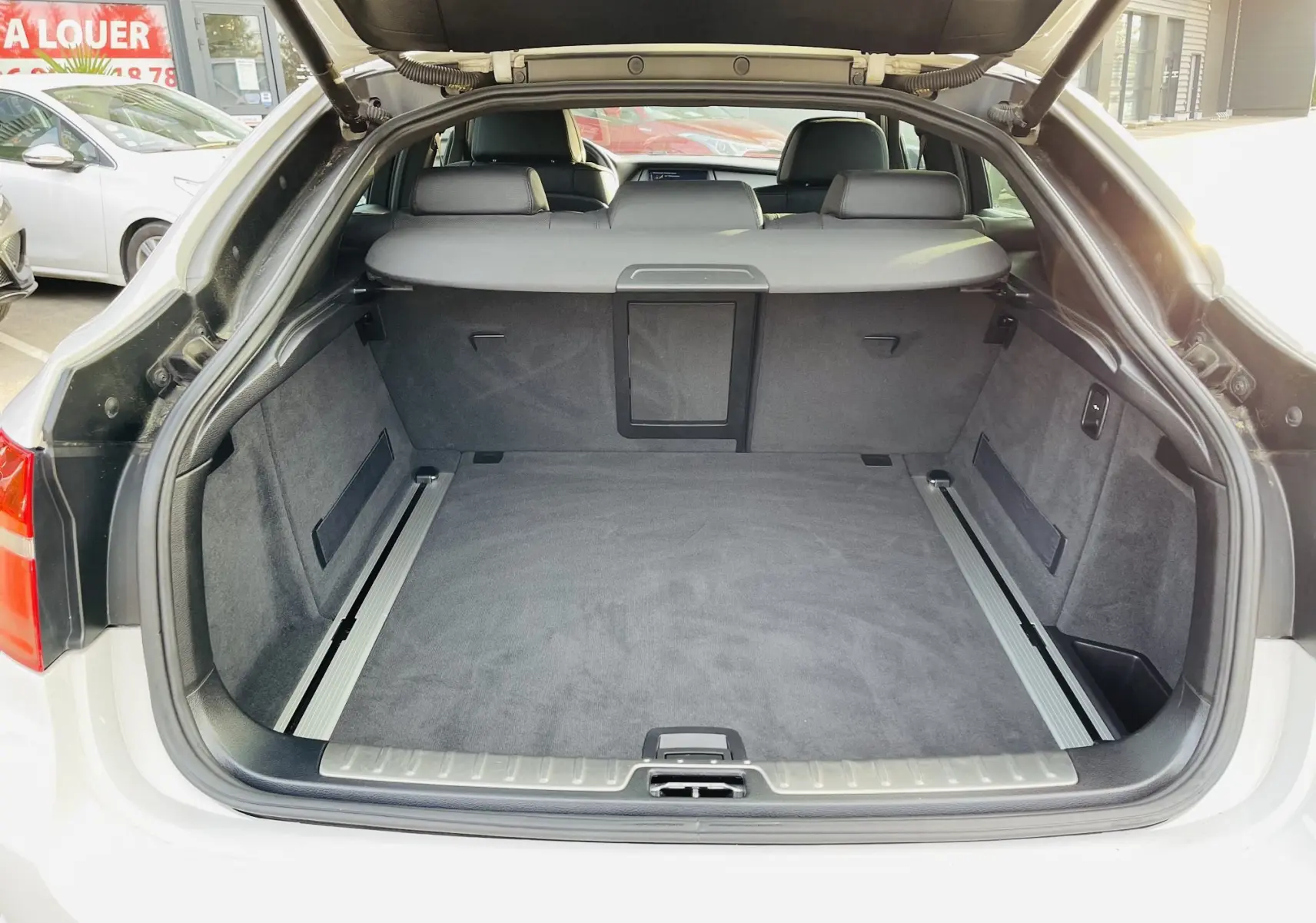 Coffre ouvert en vue arrière d'un BMW X6 blanc, montrant un espace de chargement spacieux et doublure grise.