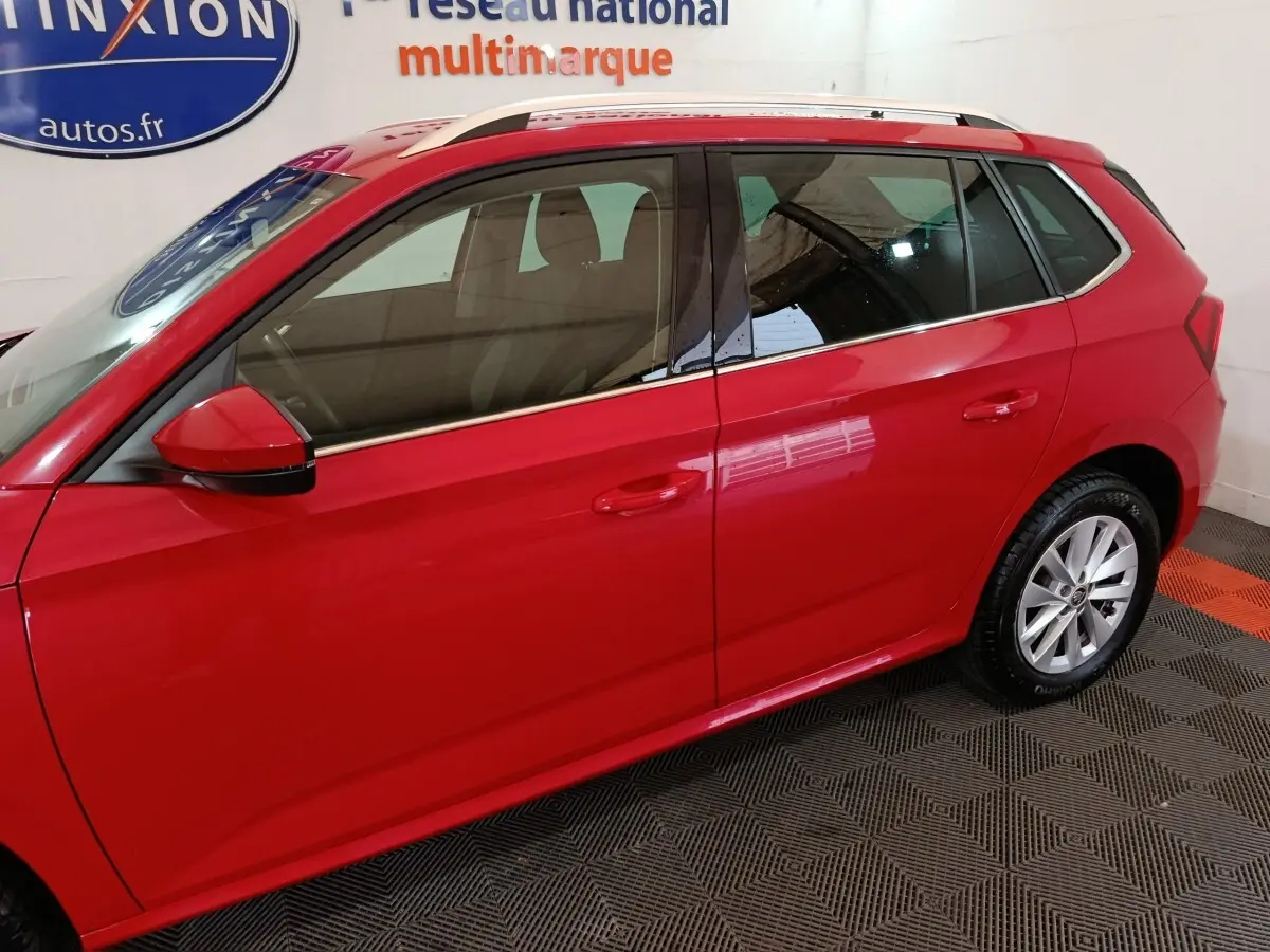 Vue latérale droite d'un Skoda Kamiq rouge 2024 avec rétroviseurs rouges et rails de toit argentés visibles.