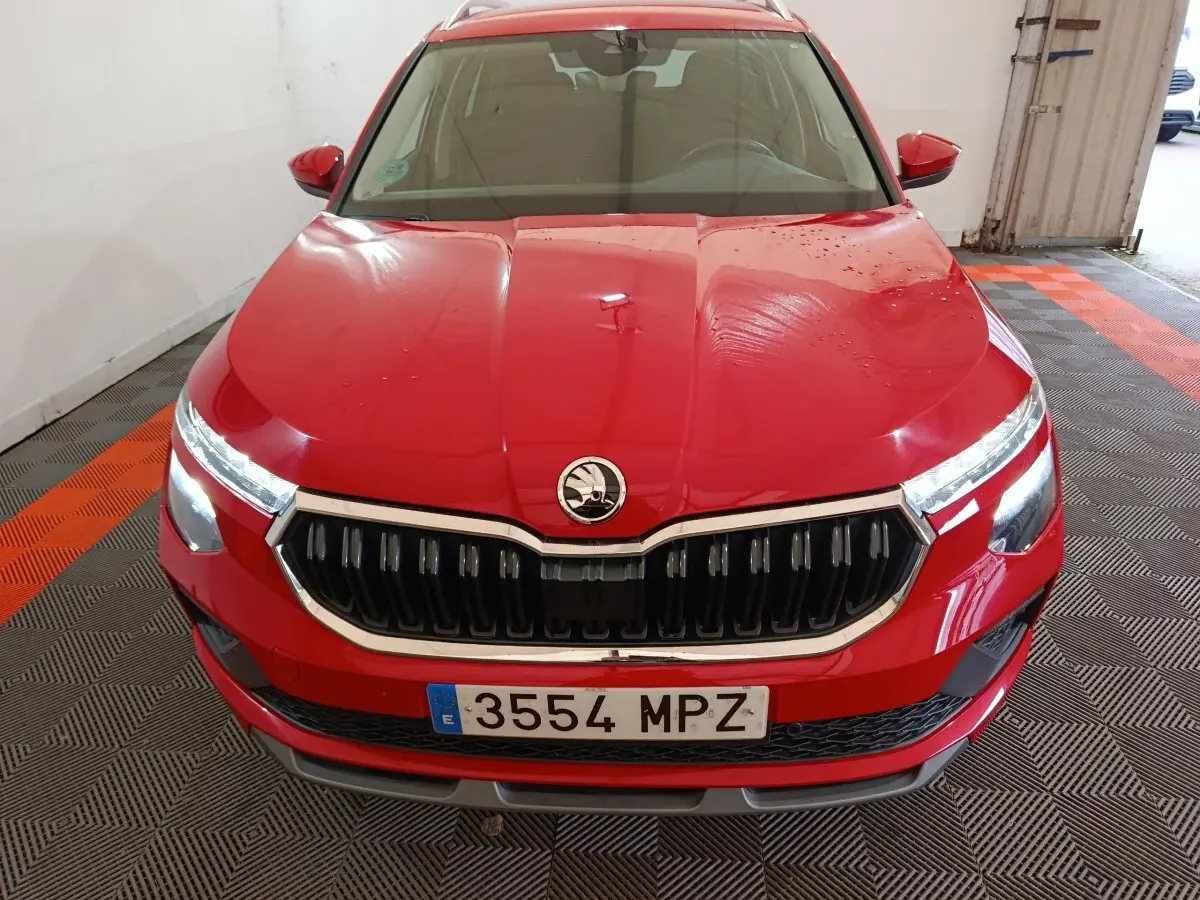 Vue avant d'un Skoda Kamiq rouge 2024 avec calandre noire et phares LED allumés dans un garage.