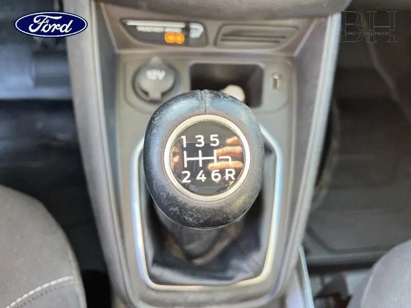 Gros plan sur le pommeau de levier de vitesse manuel noir du Ford Transit Courier Fourgon blanc, avec console centrale visible.