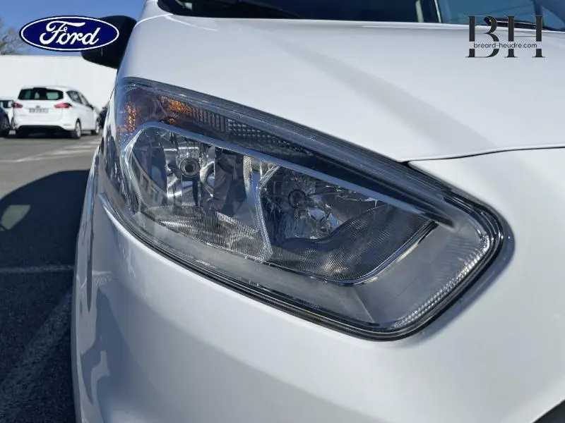 Gros plan sur le phare avant droit du Ford Transit Courier Fourgon blanc Glacier de 2019, montrant les détails du bloc optique.