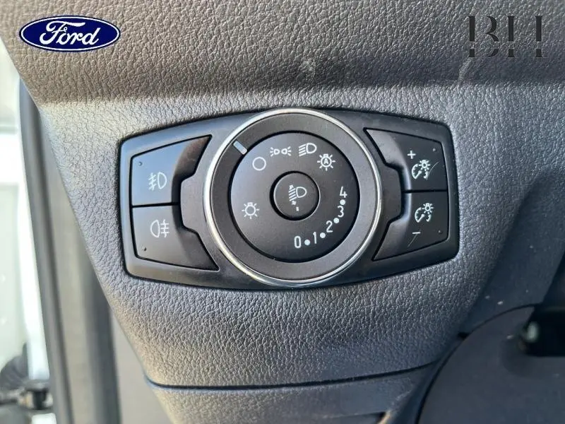 Gros plan sur la commande des phares du Ford Transit Courier Fourgon blanc Glacier, tableau de bord noir texturé.