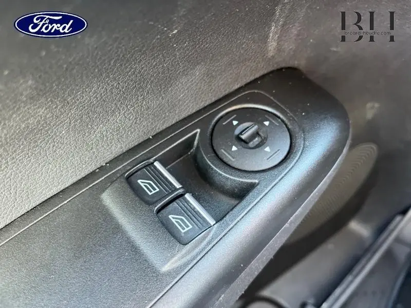 Gros plan sur les commandes électriques des vitres et réglage des rétroviseurs côté conducteur du Ford Transit Courier blanc.